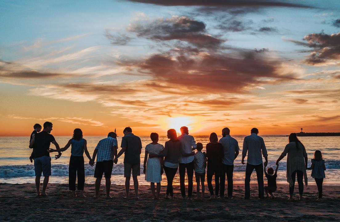 Large family stands in a line on the beach watching the sunset